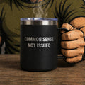Black mug with 'COMMON SENSE NOT ISSUED' text held by a person wearing a green shirt and brown gloves.