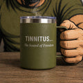 Green mug with 'Tinnitus... The Sound of Freedom' text held by a person wearing gloves.